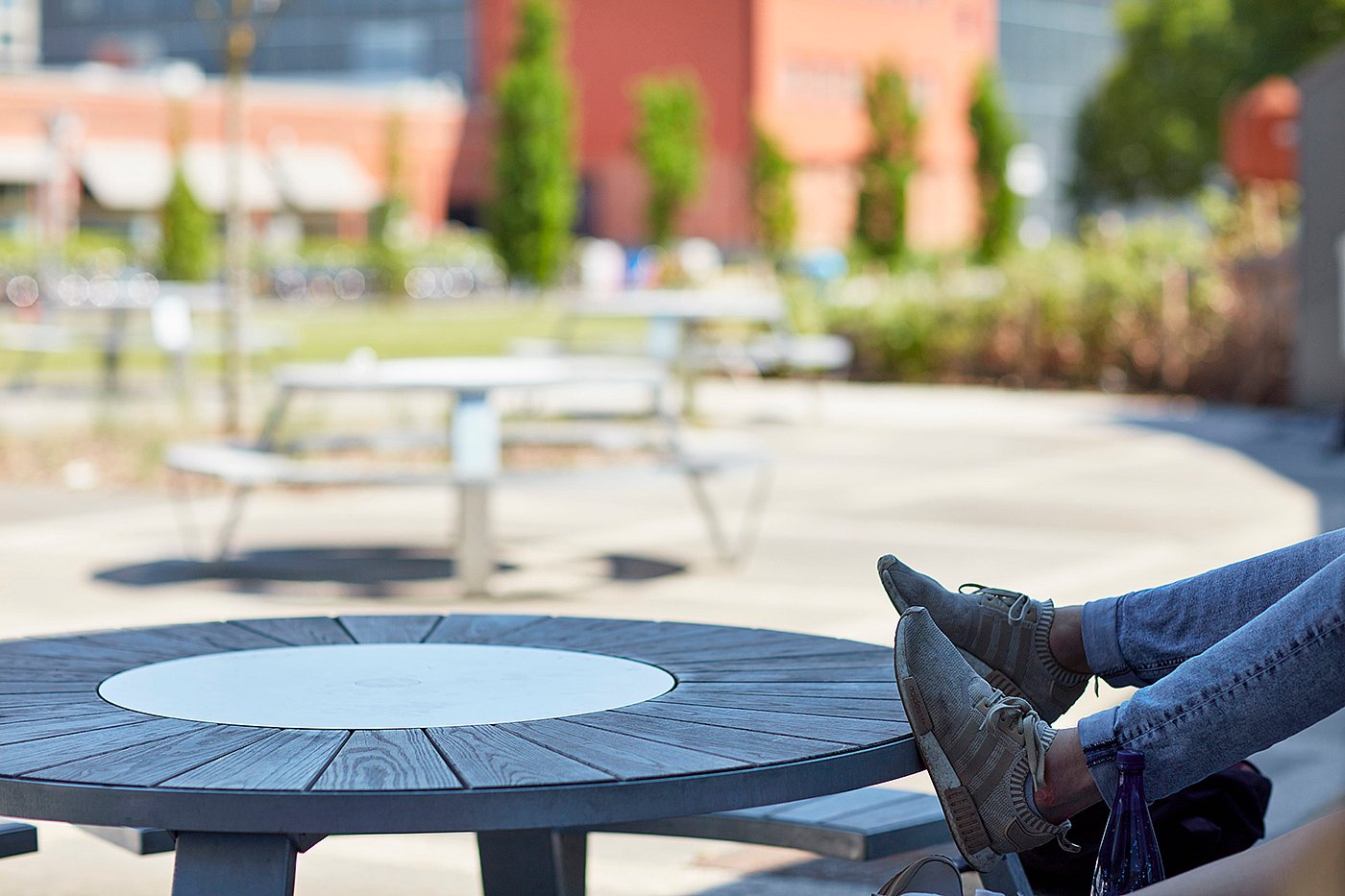 Gros plan du plateau rond en bois et du plateau tournant central d'une table de pique-nique Pantagruel, avec un étudiant allongé sur le banc incurvé.