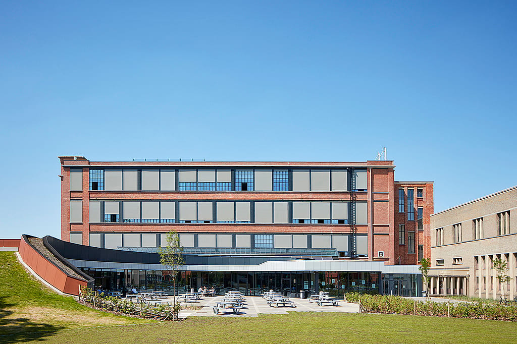 Vue extérieure large de l'Odisee University College, avec une grande terrasse équipée de tables de pique-nique Pantagruel devant le bâtiment moderne en briques et en verre.