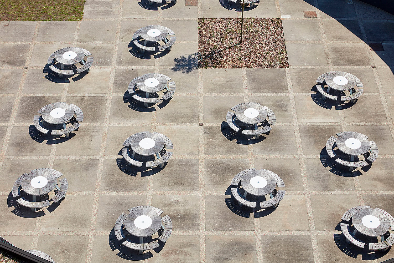 Overhead view of multiple Pantagruel picnic tables arranged across the paved terrace of Odisee University College, each with a round tabletop and curved integrated benches.