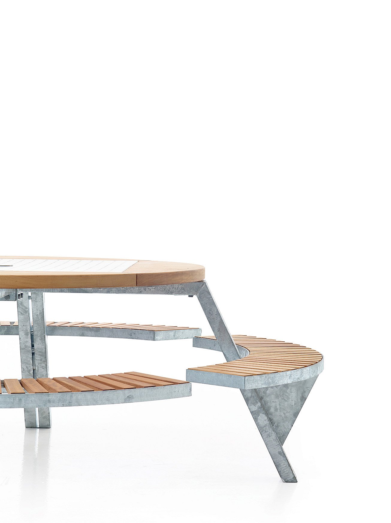   Studio close-up van de Gargantua tafel met het ronde houten tafelblad, het geperforeerde metalen middenstuk en een gebogen bank in een aangepaste zitpositie.