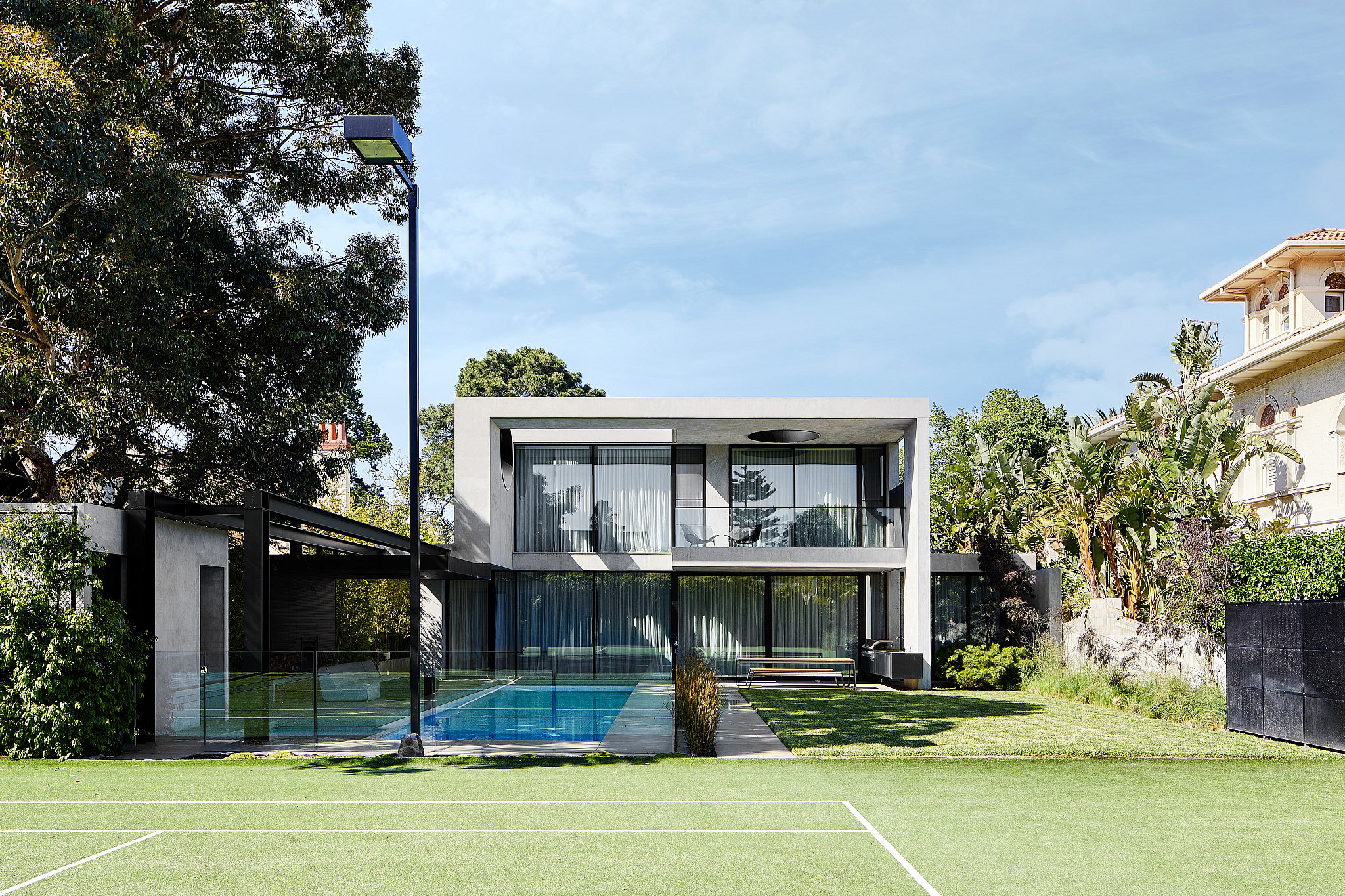 Weite Gartenansicht vom Tennisplatz zum Haus mit Blick auf den Pool, den weitläufigen Rasen und einen Hopper-Picknicktisch auf der Terrasse.