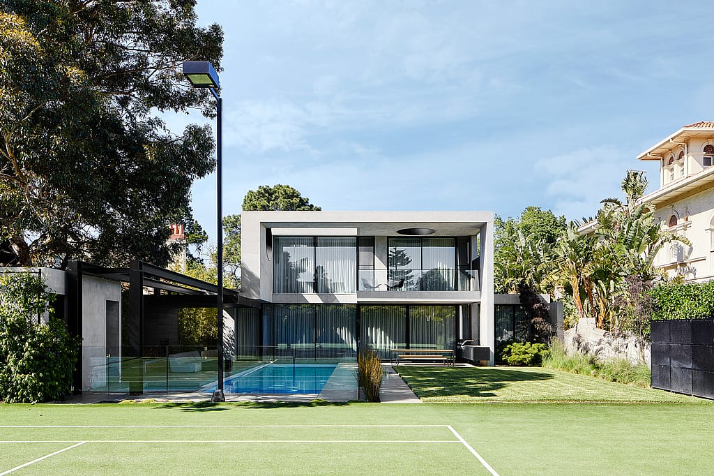 Weite Gartenansicht vom Tennisplatz zum Haus mit Blick auf den Pool, den weitläufigen Rasen und einen Hopper-Picknicktisch auf der Terrasse.