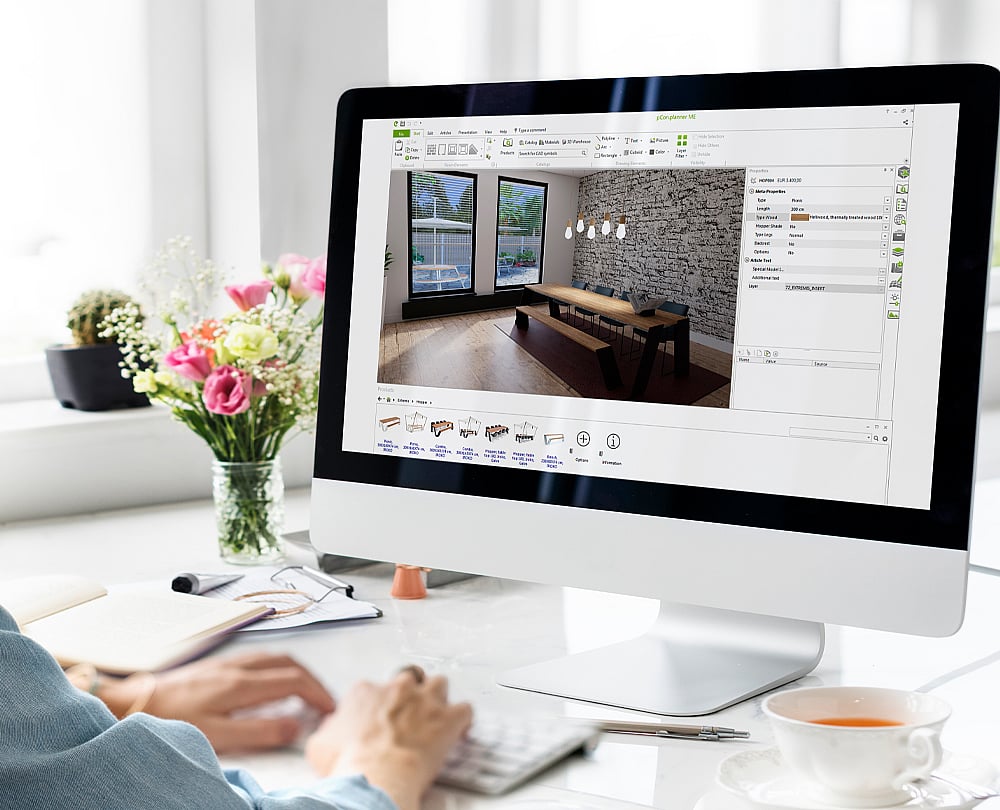 Une personne travaille sur un ordinateur de bureau affichant l'interface pCon.planner. Une table Extremis est représentée dans un intérieur lumineux, tandis que des fleurs, un carnet et une tasse de thé sont posés sur le bureau.