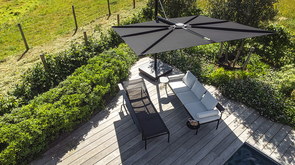 Bovenaanzicht van een houten pooldeck met een zwarte Sensu-zonnekap, witte Sol + Luna-loungestoelen en een kleine ronde bijzettafel in de hoek.