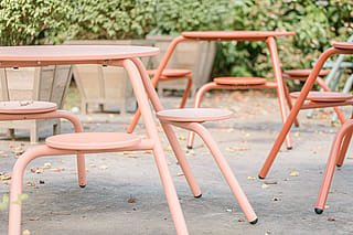 Close-up van koraalkleurige buitentafels met geïntegreerde ronde stoelen op het binnenterras.
