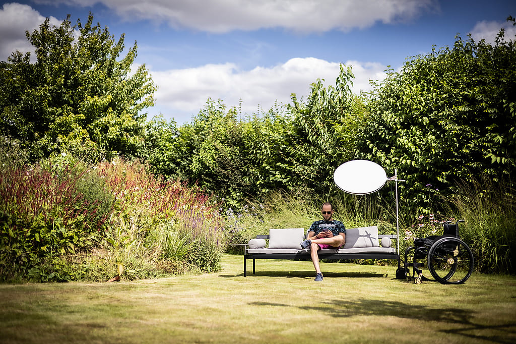 A man sits reading on a grey Sol+Luna sofa in the garden, shaded by the circular lamp.
