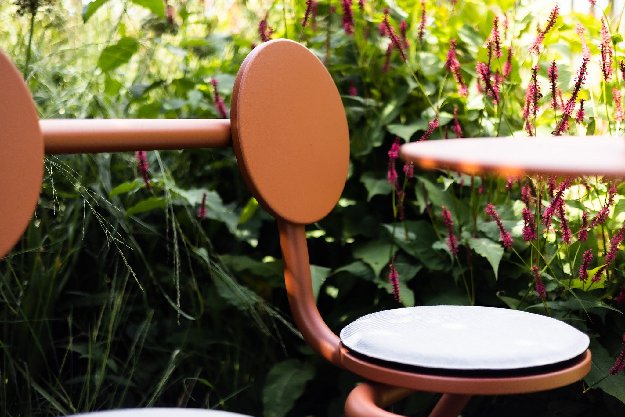 Close-up of the rounded backrest and seat cushion of a copper-brown Bistroo chair against a backdrop of pink flowers.