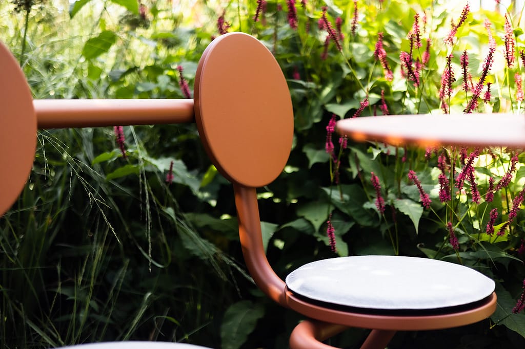 Close-up of the rounded backrest and seat cushion of a copper-brown Bistroo chair against a backdrop of pink flowers.