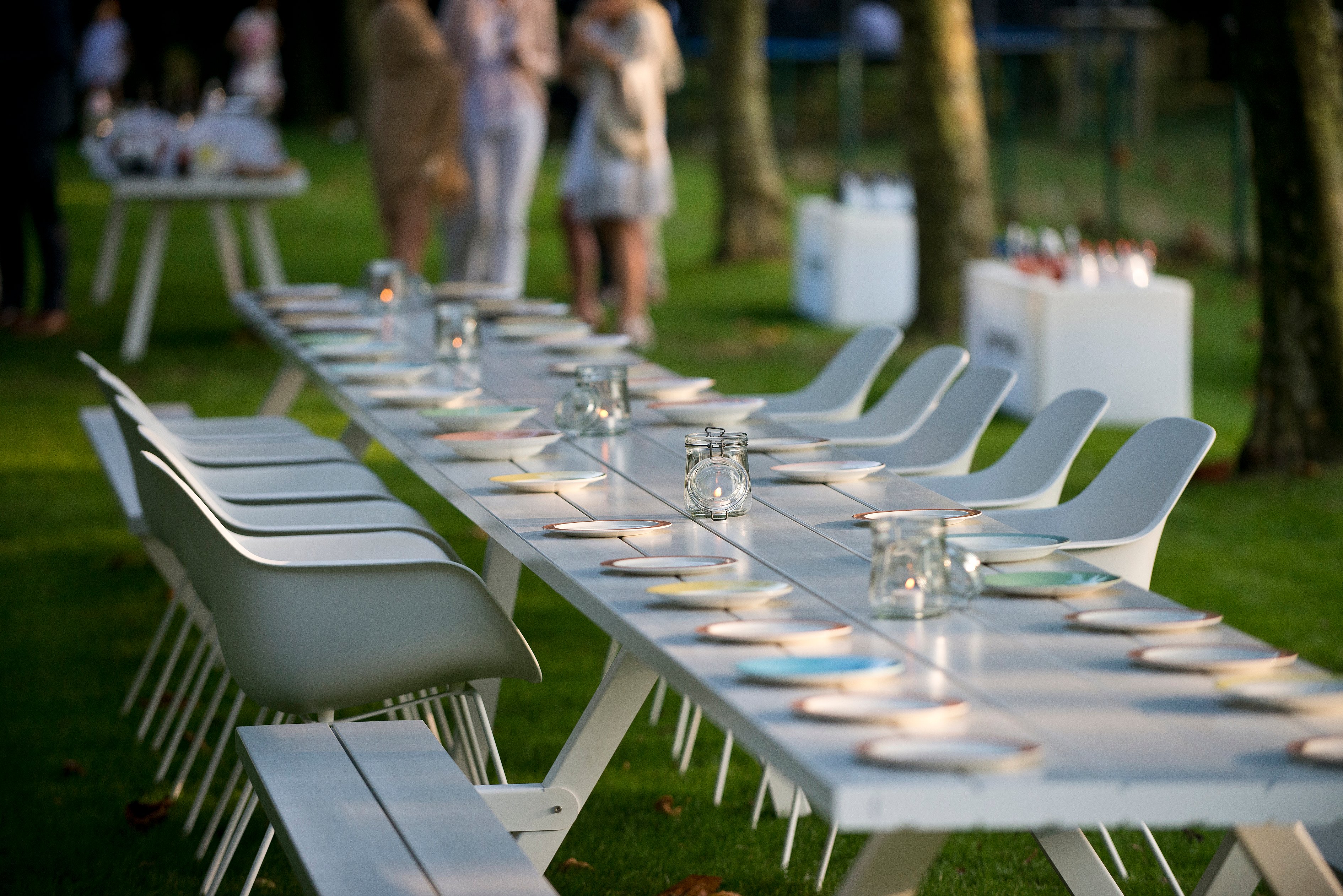 Seitenansicht des langen weißen Marina-Kombitisches mit weißen Kapitänsstühlen für ein Abendessen im Freien auf dem Rasen.