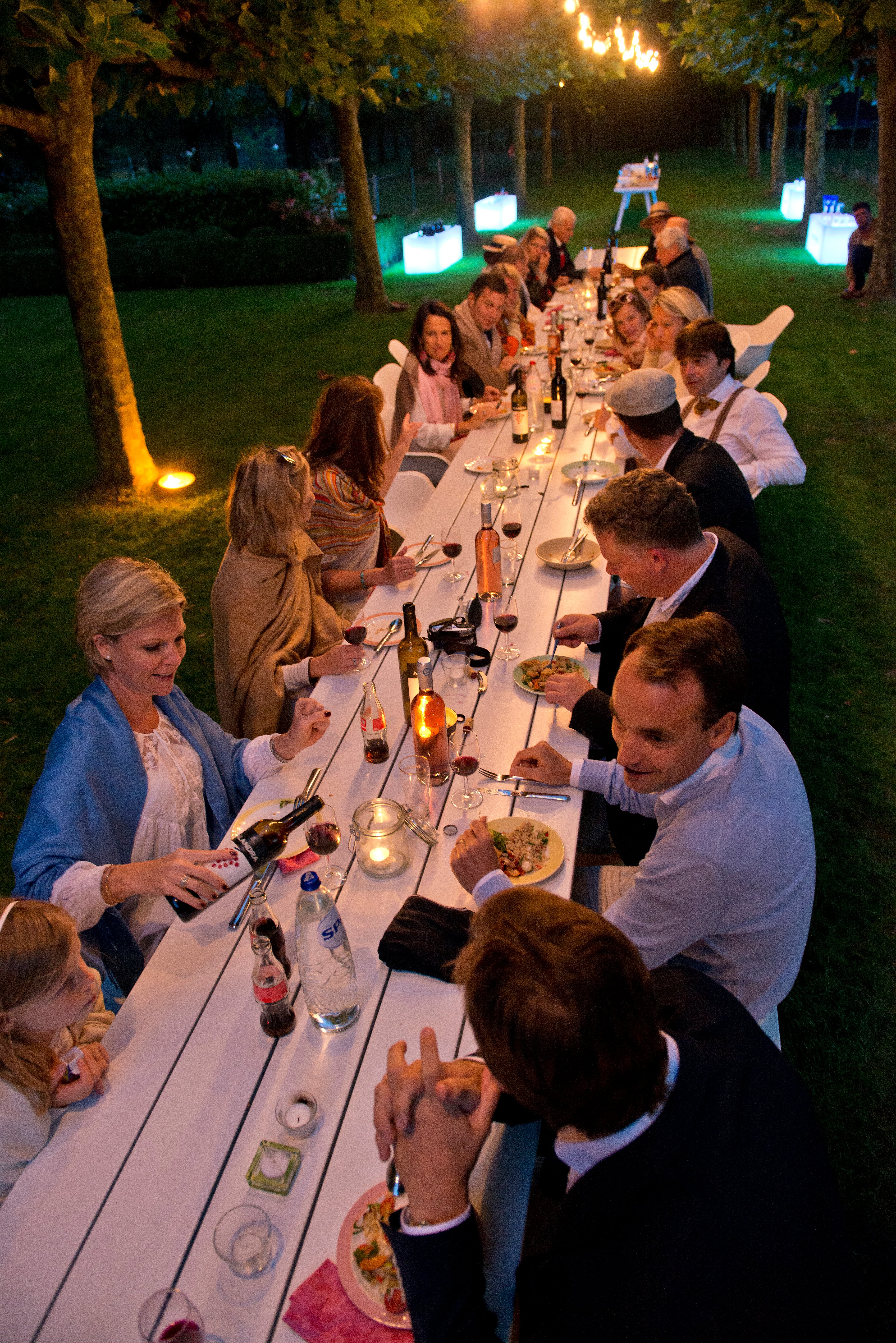 Draufsicht auf Familie und Freunde beim gemeinsamen Abendessen, Wein und Gespräch entlang der gesamten Länge des weißen Marina-Kombitisches.