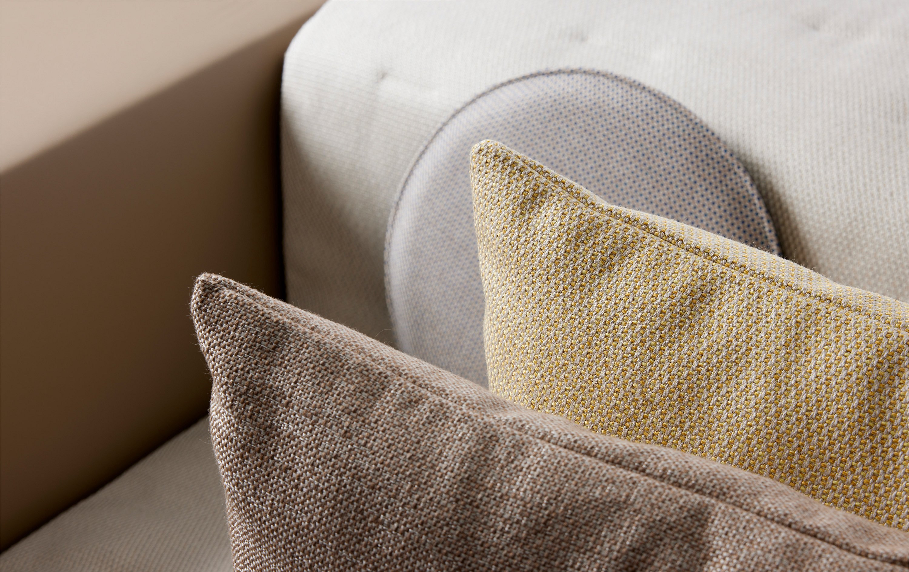 Gros plan sur des coussins d’extérieur texturés en tissus neutres beige, jaune et bleu clair superposés sur un canapé.