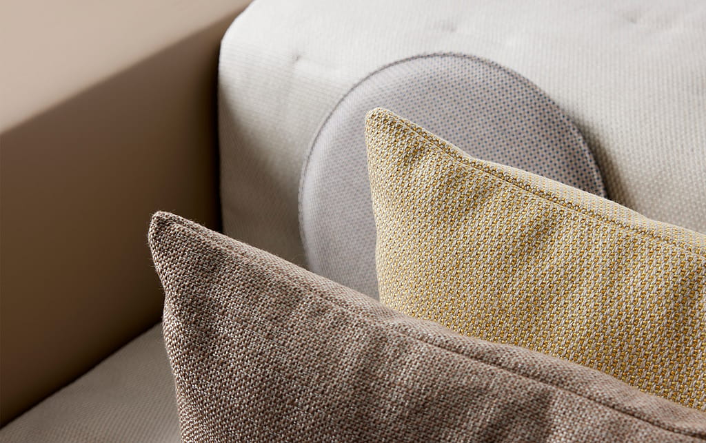 Close-up of textured outdoor cushions in neutral beige, yellow, and light blue fabrics layered on a sofa.