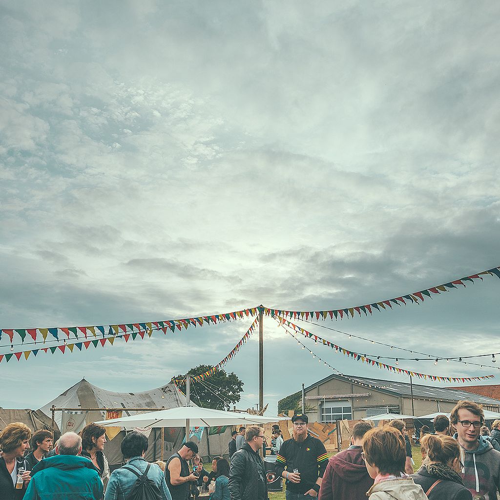 Bei einem Festival im Freien versammelten sich Menschenmengen unter bunten Wimpel- und Lichterketten unter bewölktem Himmel.