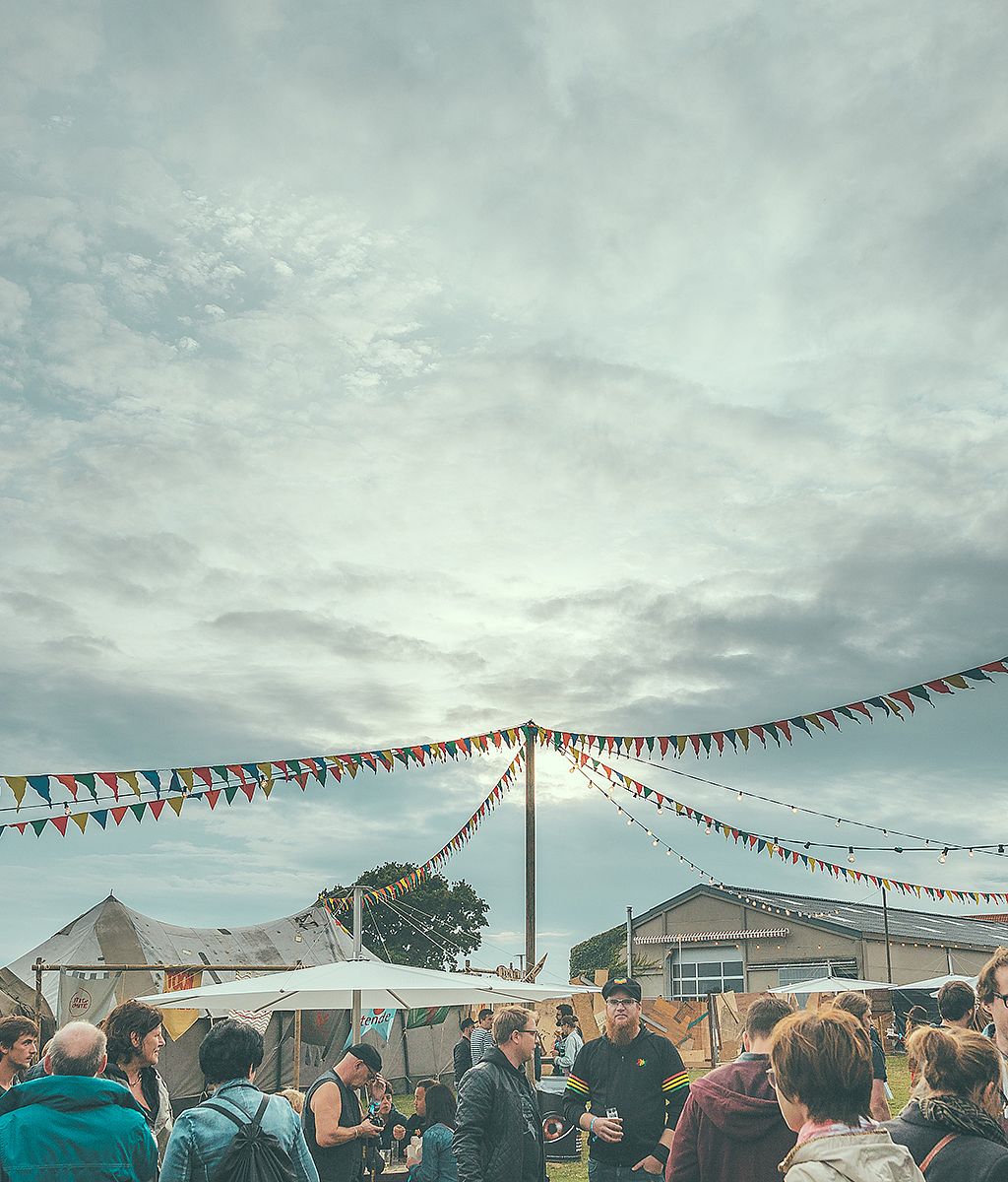 Bei einem Festival im Freien versammelten sich Menschenmengen unter bunten Wimpel- und Lichterketten unter bewölktem Himmel.