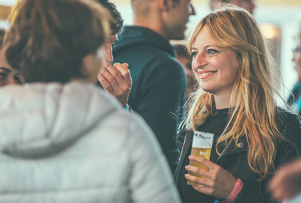 Lächelnde Frau hält ein Glas Bier in der Hand, während sie mit anderen Festivalgästen plaudert.