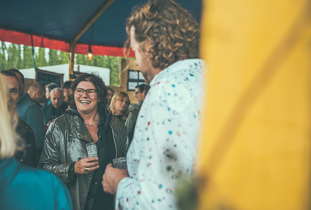 Frau lacht mit einem Drink in der Hand, während sie unter dem Festzelt redet.
