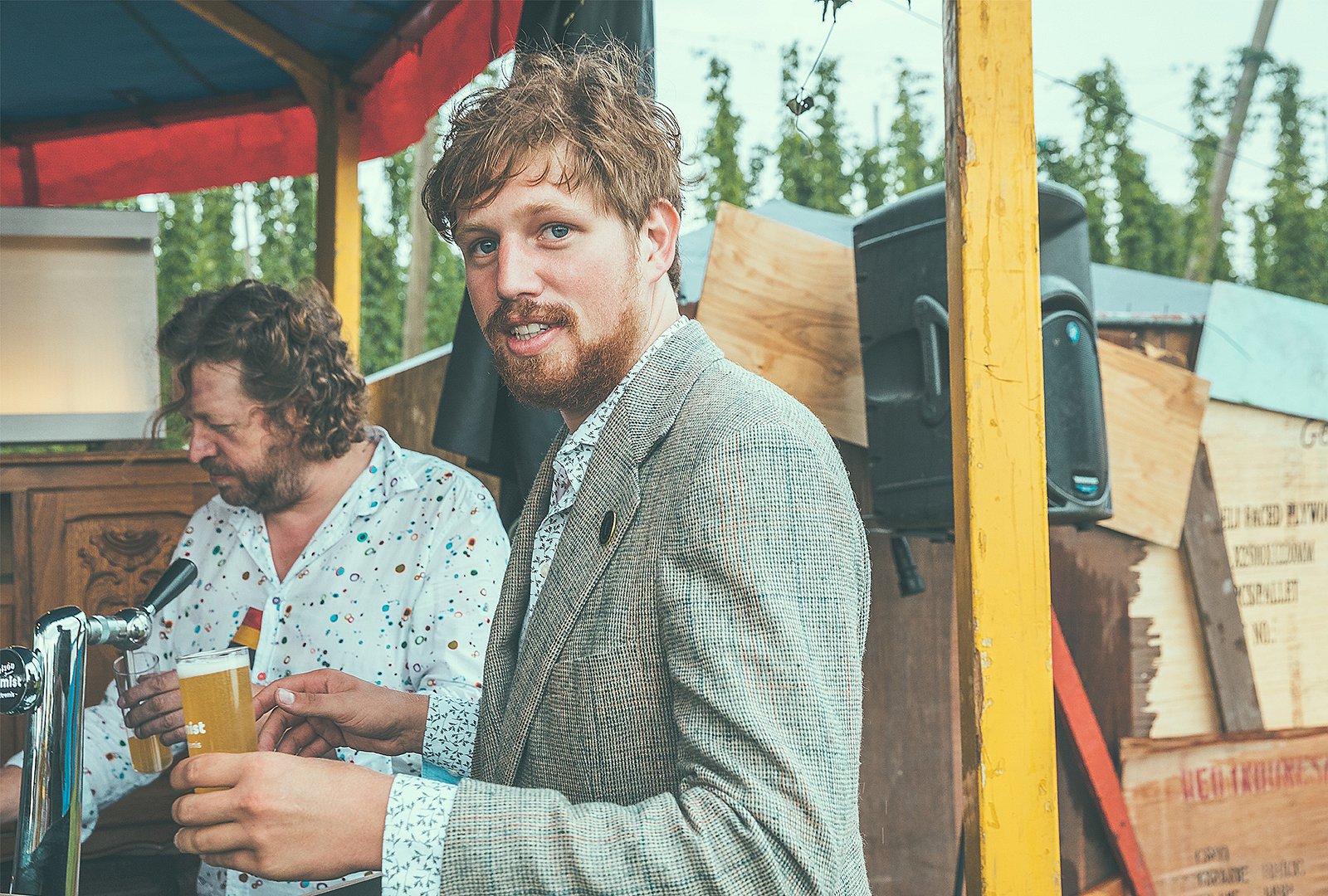 Thomas in einem Blazer hält ein Glas Bier neben dem Zapfhahn, hinter ihm gießt ein anderer Mann Bier ein.