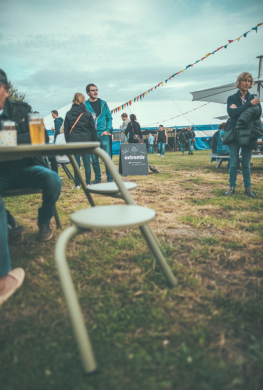 Flachwinkelansicht der Außenhocker im Vordergrund mit Festivalbesuchern und einem Extremis-Schild in der Ferne.