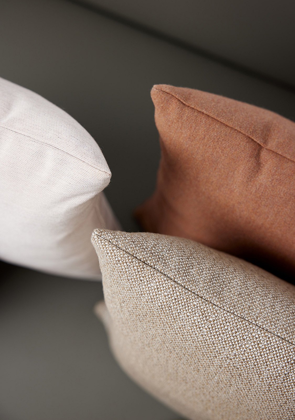 Close-up van drie geweven kussens in gebroken witte, beige en terracotta tinten.