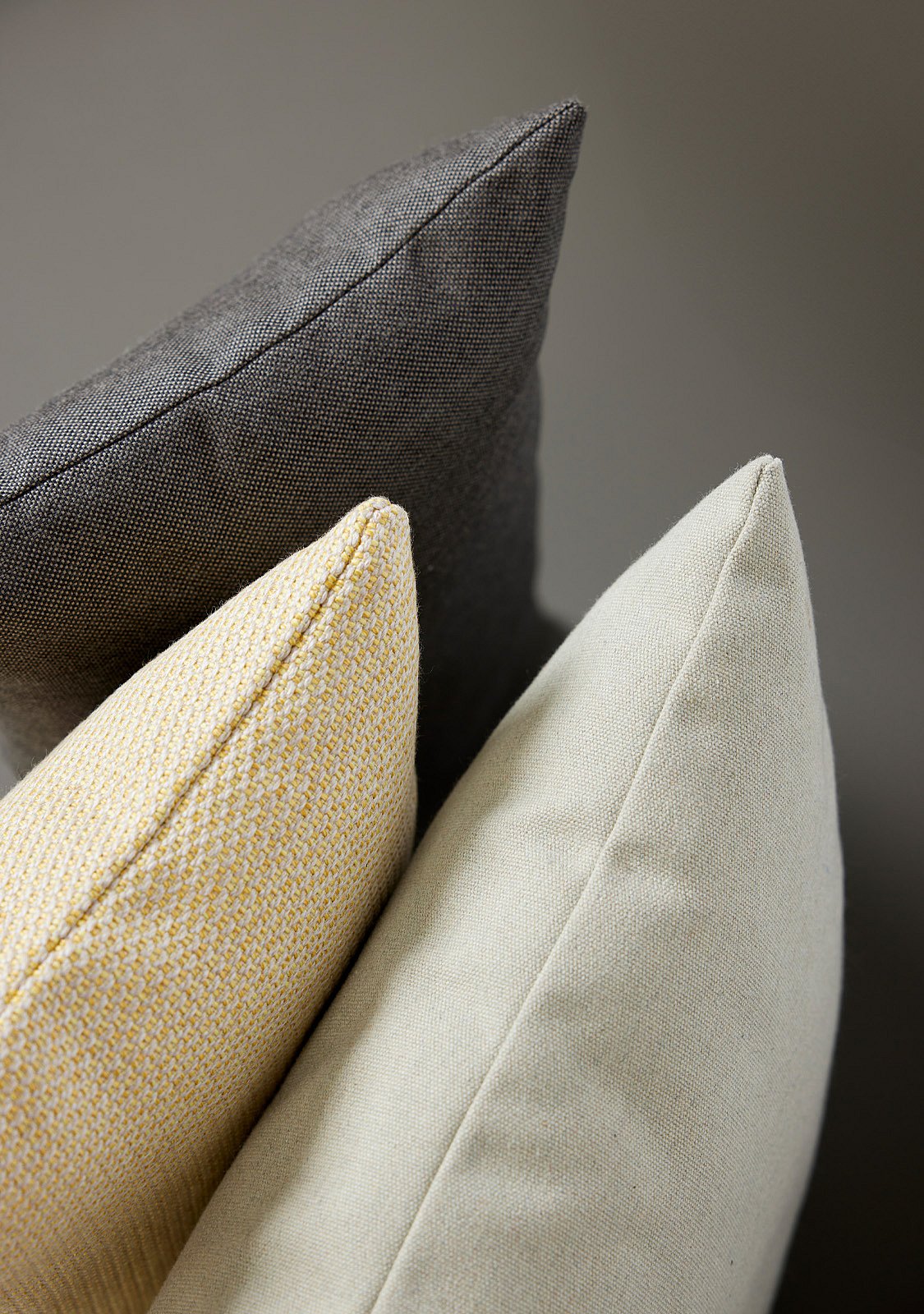 Close-up van drie geweven kussens in houtskool, zachtgeel en lichtbeige