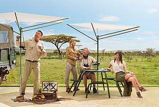 Un parasol Acacia blanc surplombe une table ronde compacte blanche de style « virus », avec ses sièges intégrés. Des haies et des arbres se détachent en arrière-plan.