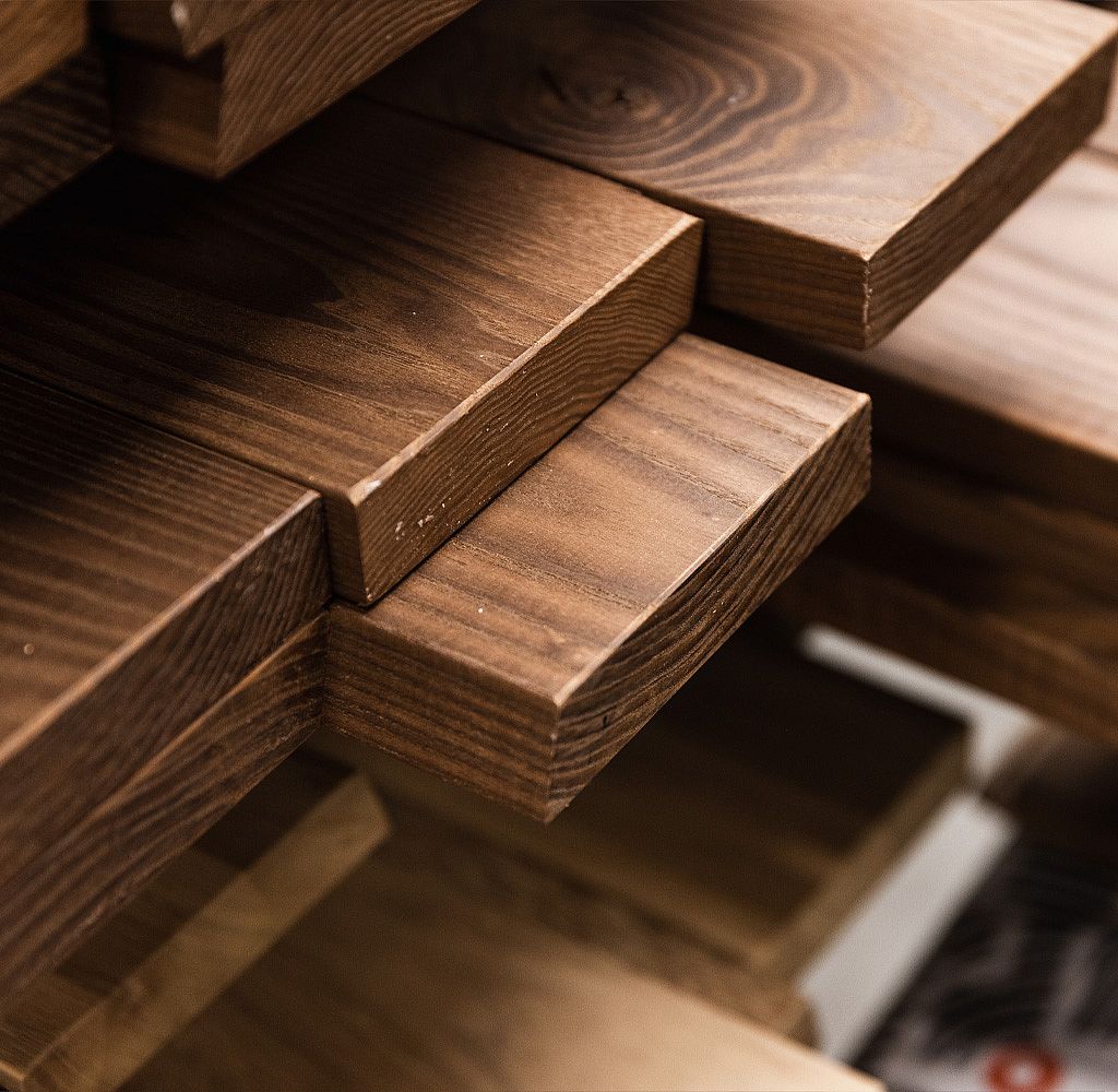Gros plan sur des lattes de table empilées en bois foncé avec un grain visible et des bords arrondis, mettant l’accent sur le savoir-faire et le parcours du bois brut au mobilier fini.