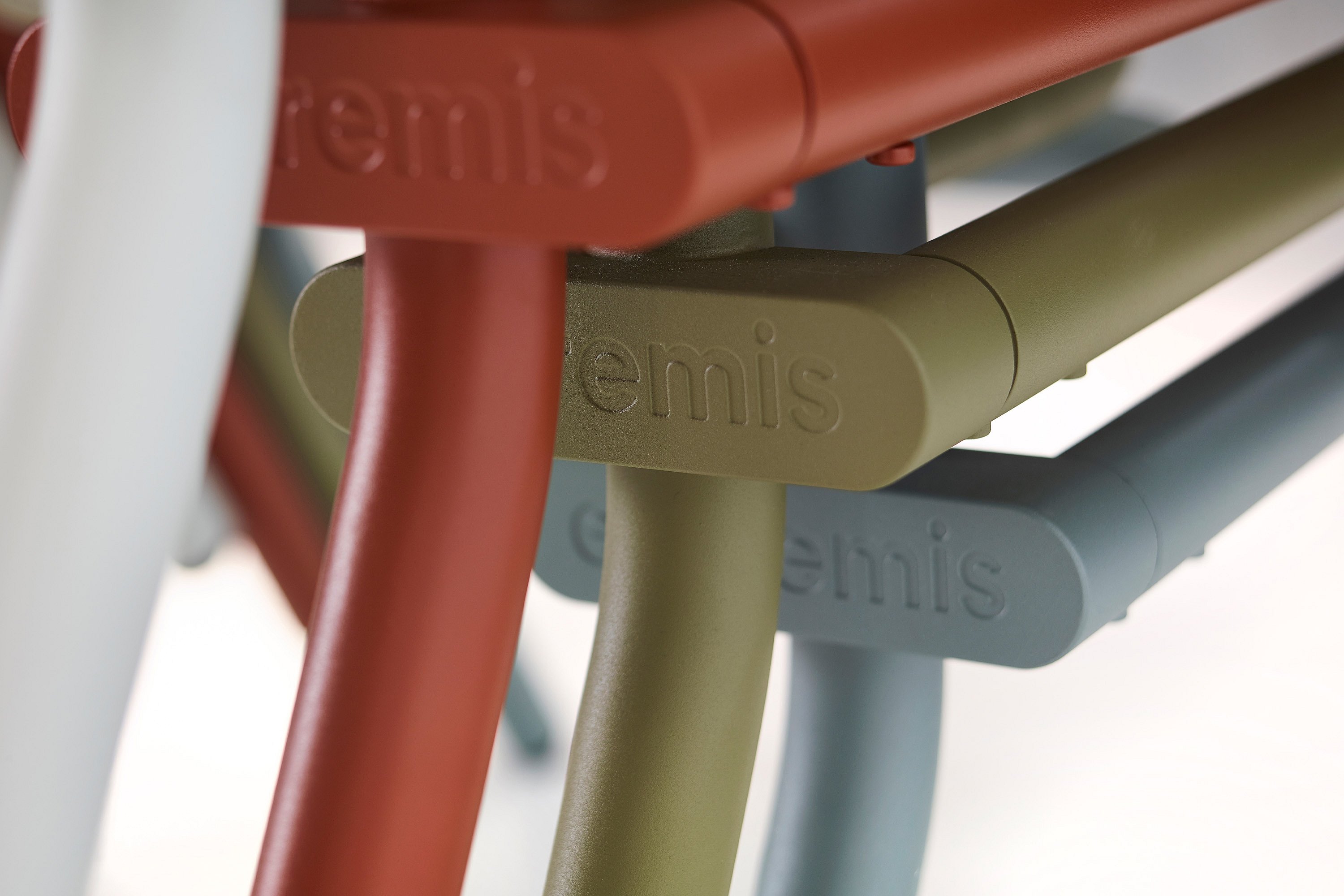   Empilement de structures métalliques de chaises ou de tabourets, de couleur rouge rouille, vert olive et bleu clair, chacune portant en relief une partie du nom Extremis.