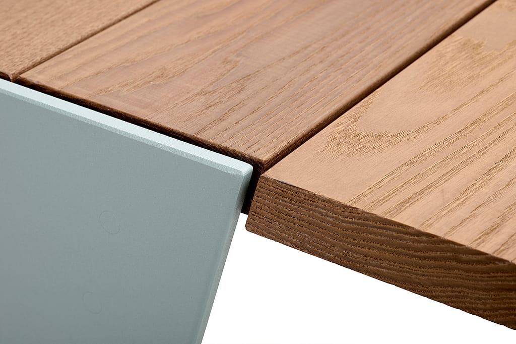 Détail d'un plateau de table rond en bois avec un rebord métallique vert pâle et un pied incliné, mettant en valeur le bord incurvé et l'assemblage.