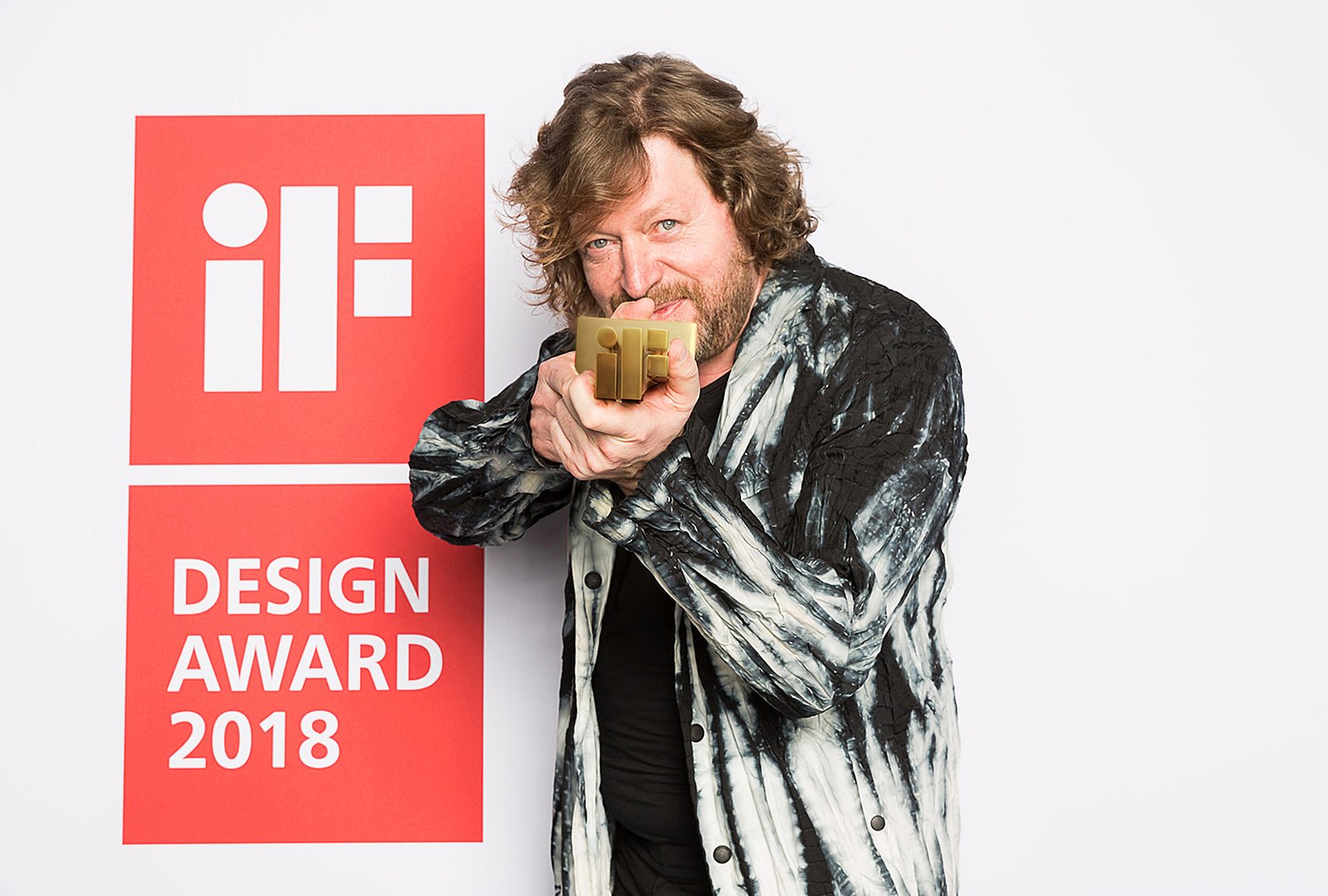 Man holding a gold iF award trophy toward the camera while standing beside a large red iF Design Award 2018 sign.