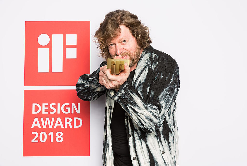 Homme tenant un trophée d’or du prix iF vers la caméra, debout à côté d’une grande pancarte rouge du prix iF Design Award 2018.