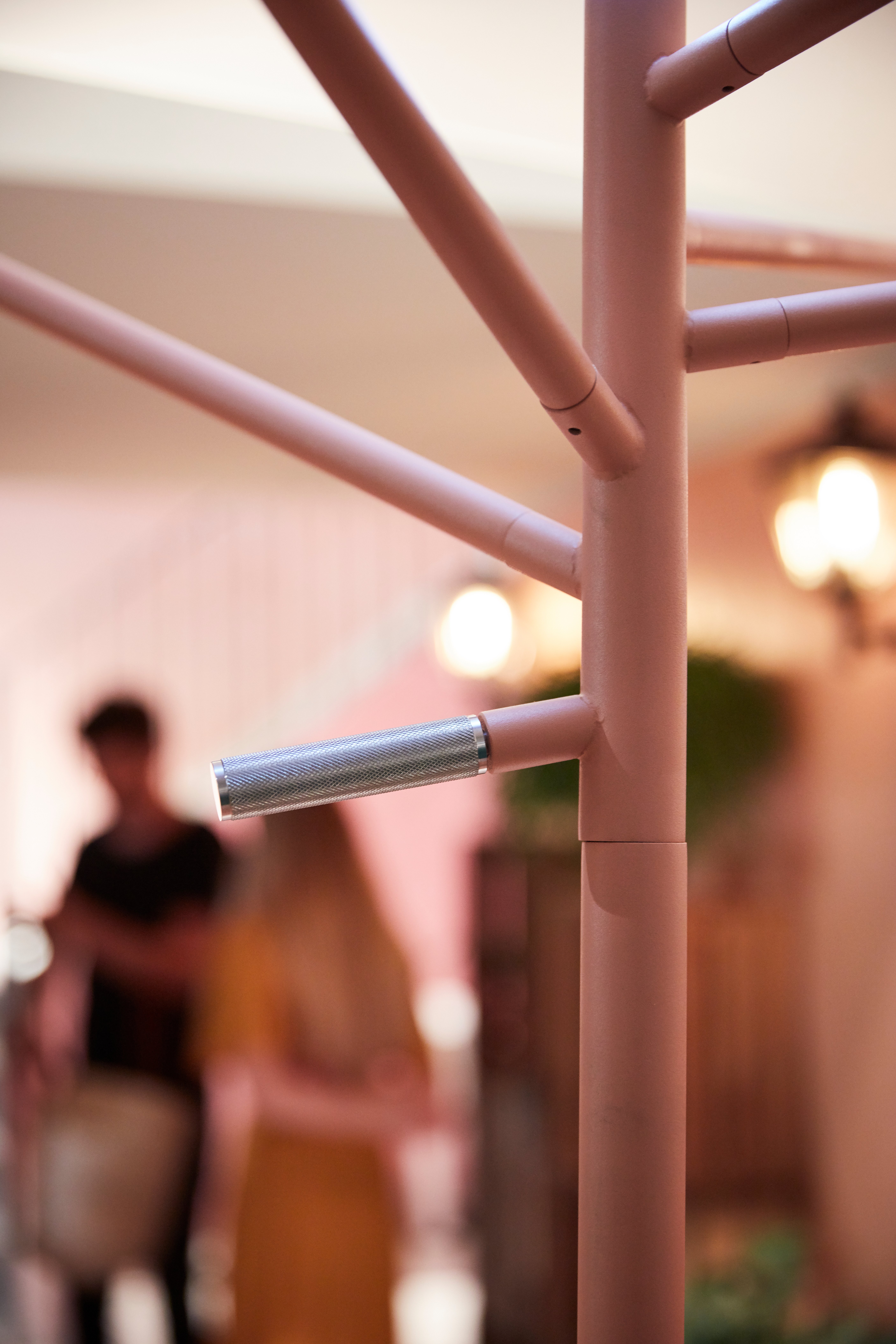 Close-up of the pink Acacia parasol pole and branching arm structure with the exhibition scene softly blurred behind it.