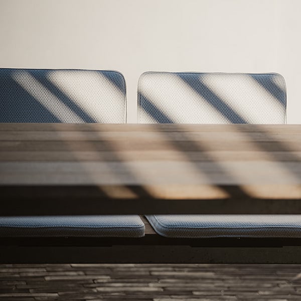 Deux sièges BYOS rembourrés, fixés de part et d'autre de bancs Hopper, sont visibles juste au-dessus du plateau de la table. Des ombres rayées les traversent.