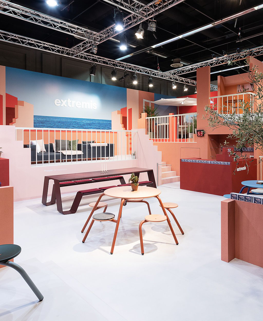 Vue d’ensemble du stand d’exposition Extremis IMM 2020 aux tons pastel, avec des terrasses, des escaliers, des balcons et de multiples meubles disposés comme une scène intérieure d’inspiration méditerranéenne.