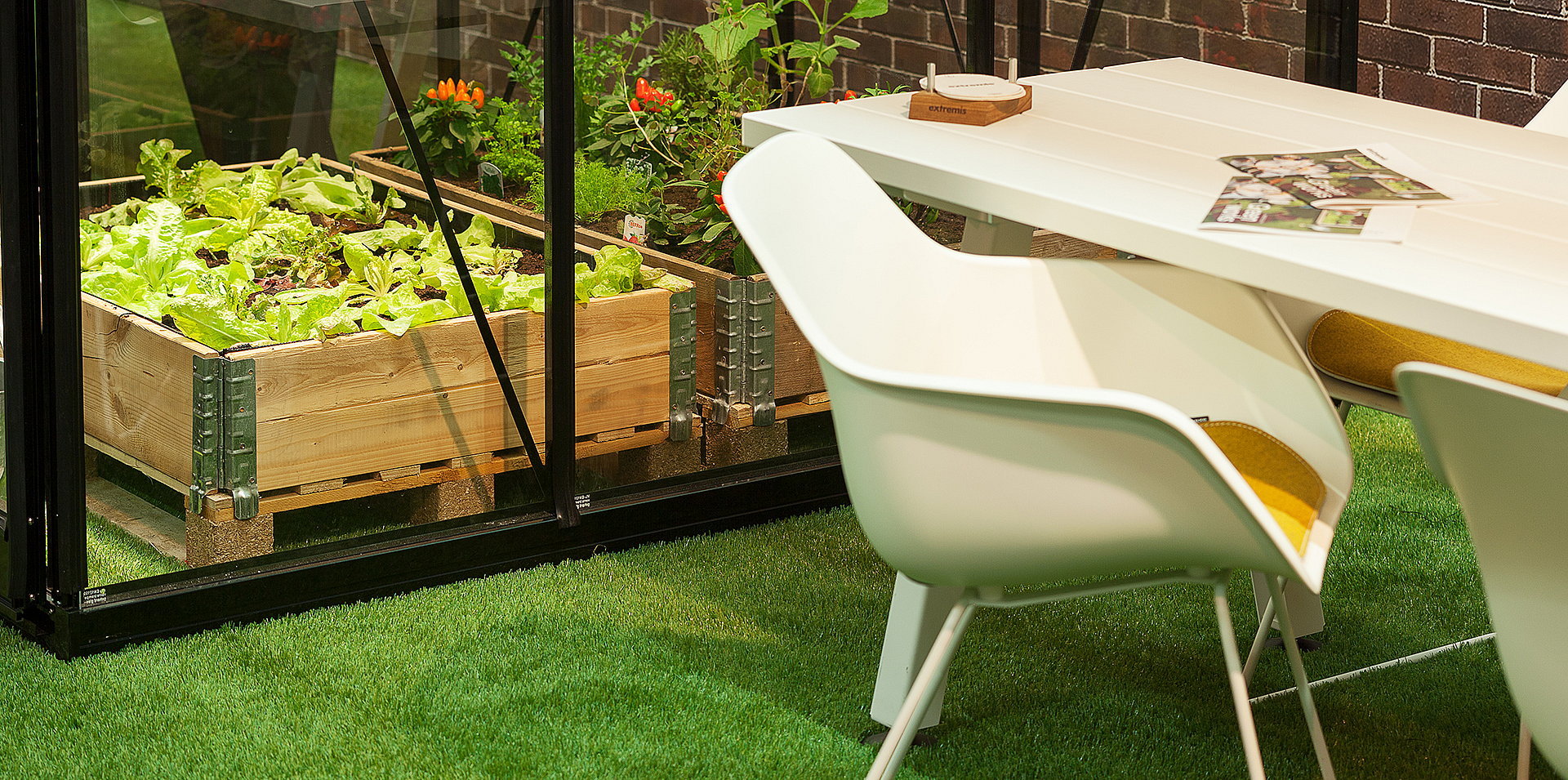 Gros plan d’une haute chaise de capitaine blanche à côté d’un plateau en bois pâle sur gazon artificiel, mettant en valeur la fine structure métallique et l’assise incurvée.