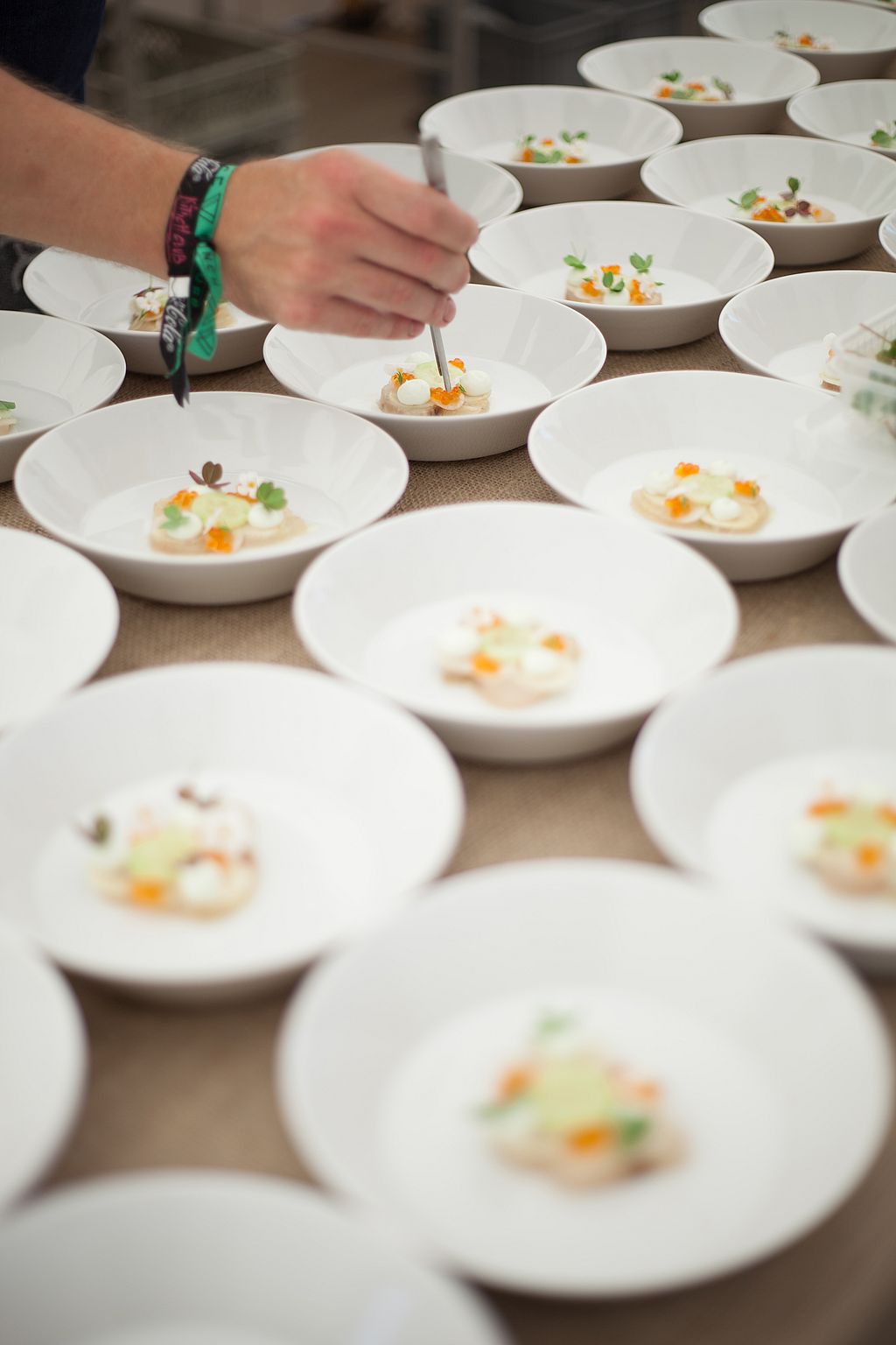 Un chef dresse de petites assiettes composées dans une rangée de bols blancs avant le service.