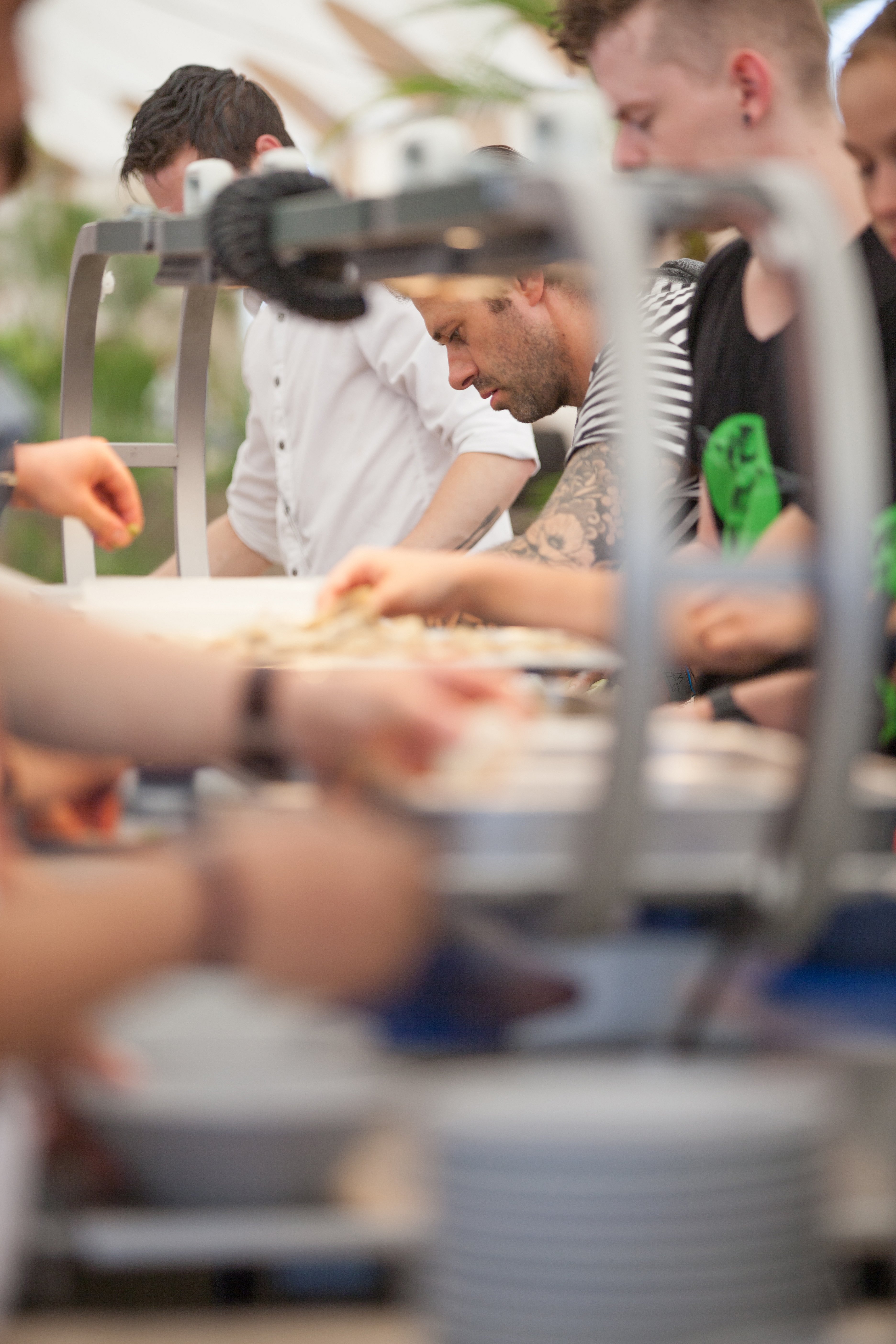   Des cuisiniers s'affairent derrière un comptoir de buffet, visibles à travers le flou des ustensiles de service au premier plan.