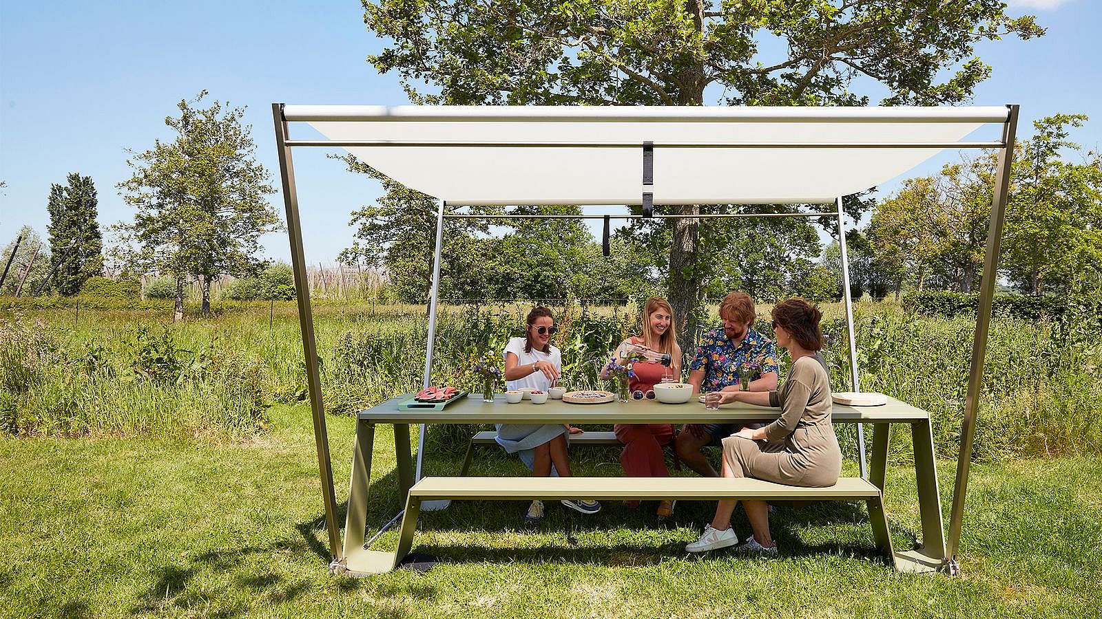 Des amis profitant de leur nourriture à la table à provisions, bien protégés du soleil sous l’ombre de la trémie.
