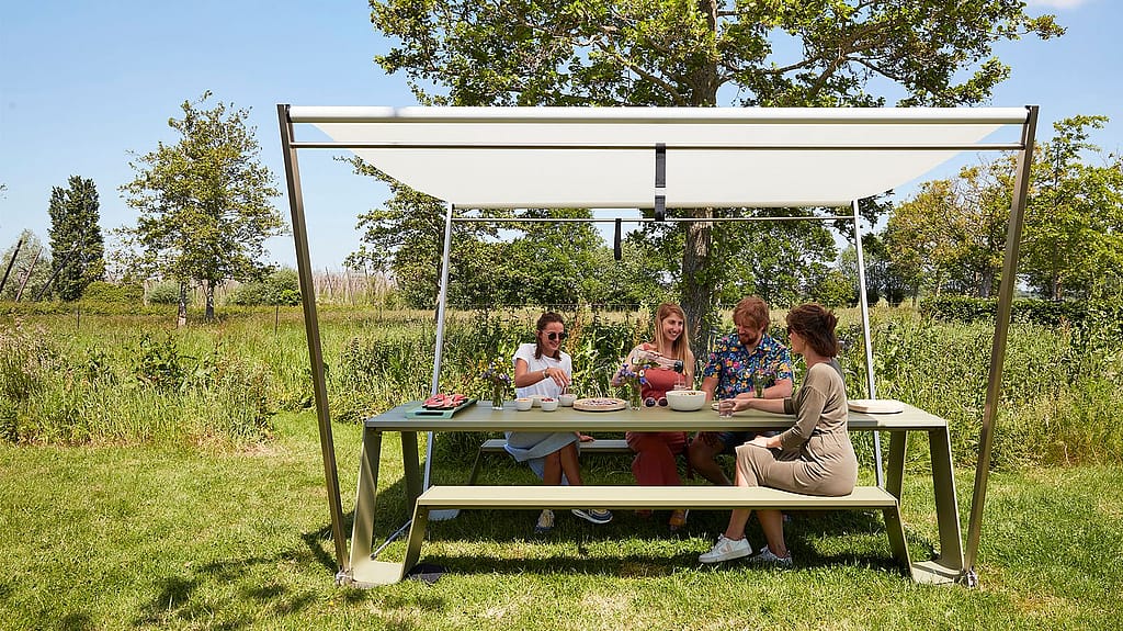 Des amis profitant de leur nourriture à la table à provisions, bien protégés du soleil sous l’ombre de la trémie.