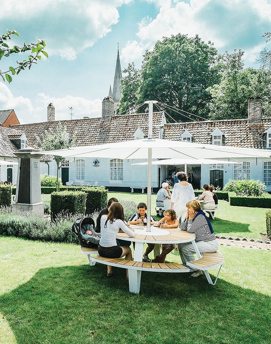 Des amis assis ensemble à la table pantagruel moderne par un temps magnifique tout en étant protégés du soleil grâce au parasol inumbra offrant suffisamment d’ombre pour que tout le monde puisse en profiter.