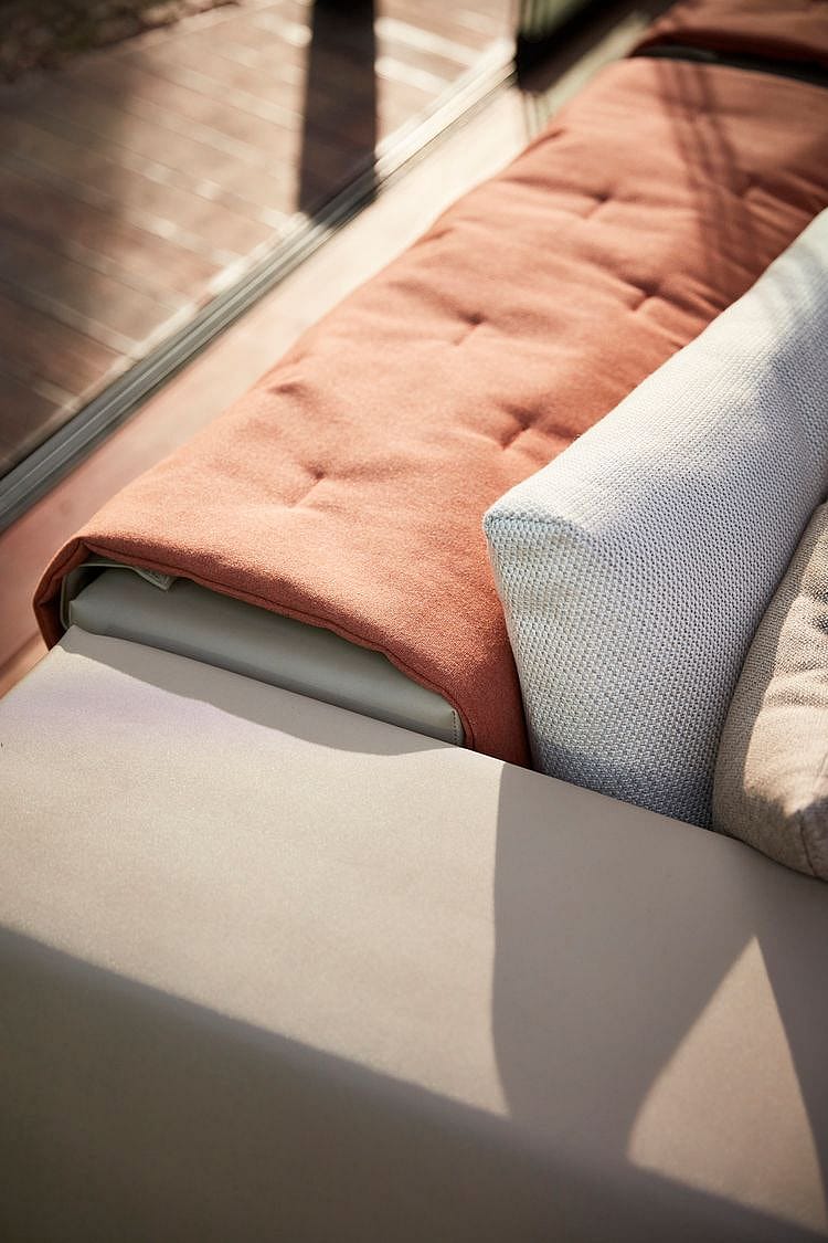 Nahaufnahme einer Walrus-Sofaecke mit einer terrakottafarbenen Sitzdecke und einem hellen, strukturierten Lendenkissen im warmen Sonnenlicht.