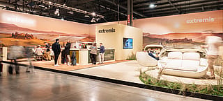 Breed uitzicht op de Extremis-stand in Salone del Mobile, met een panoramische Toscaanse heuvelachtergrond, een receptieteller, bezoekers en Cabrio-banken in een met gras begroeide omgeving.