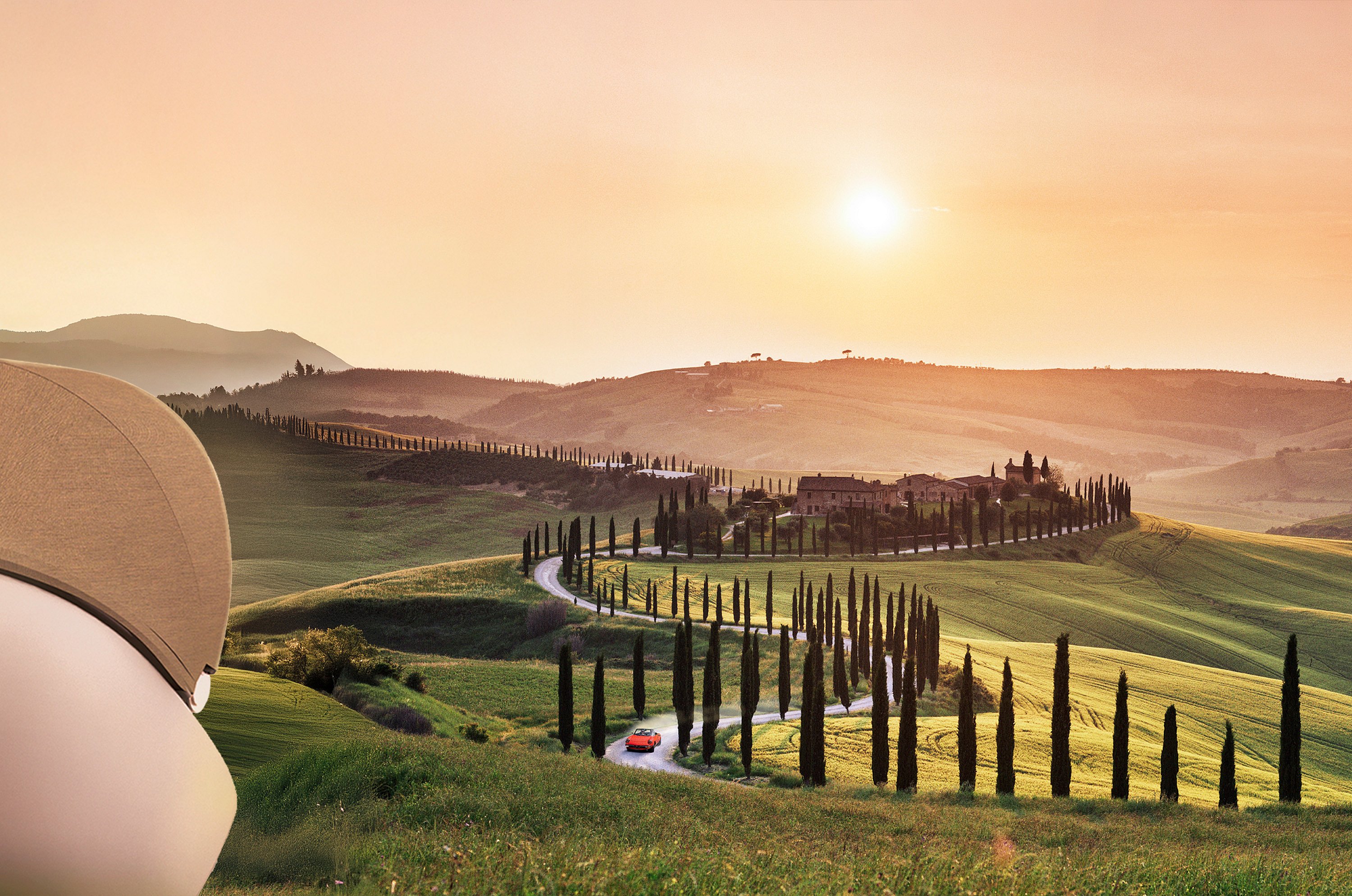 Zonverlicht Toscaans landschap met glooiende heuvels, een kronkelende met cipressen omzoomde weg en een kleine rode cabriolet die naar een boerderij op een heuveltop rijdt.