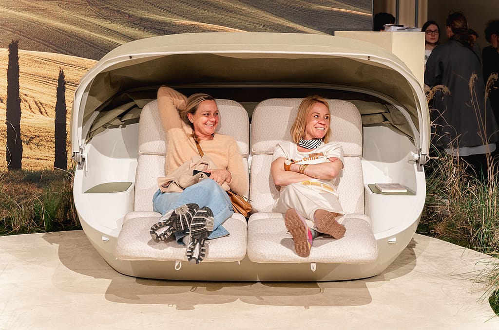 Twee vrouwen ontspannen naast elkaar in een crèmekleurige cabriobank met het baldakijn omhoog en kleine bijzettafeltjes aan beide uiteinden.