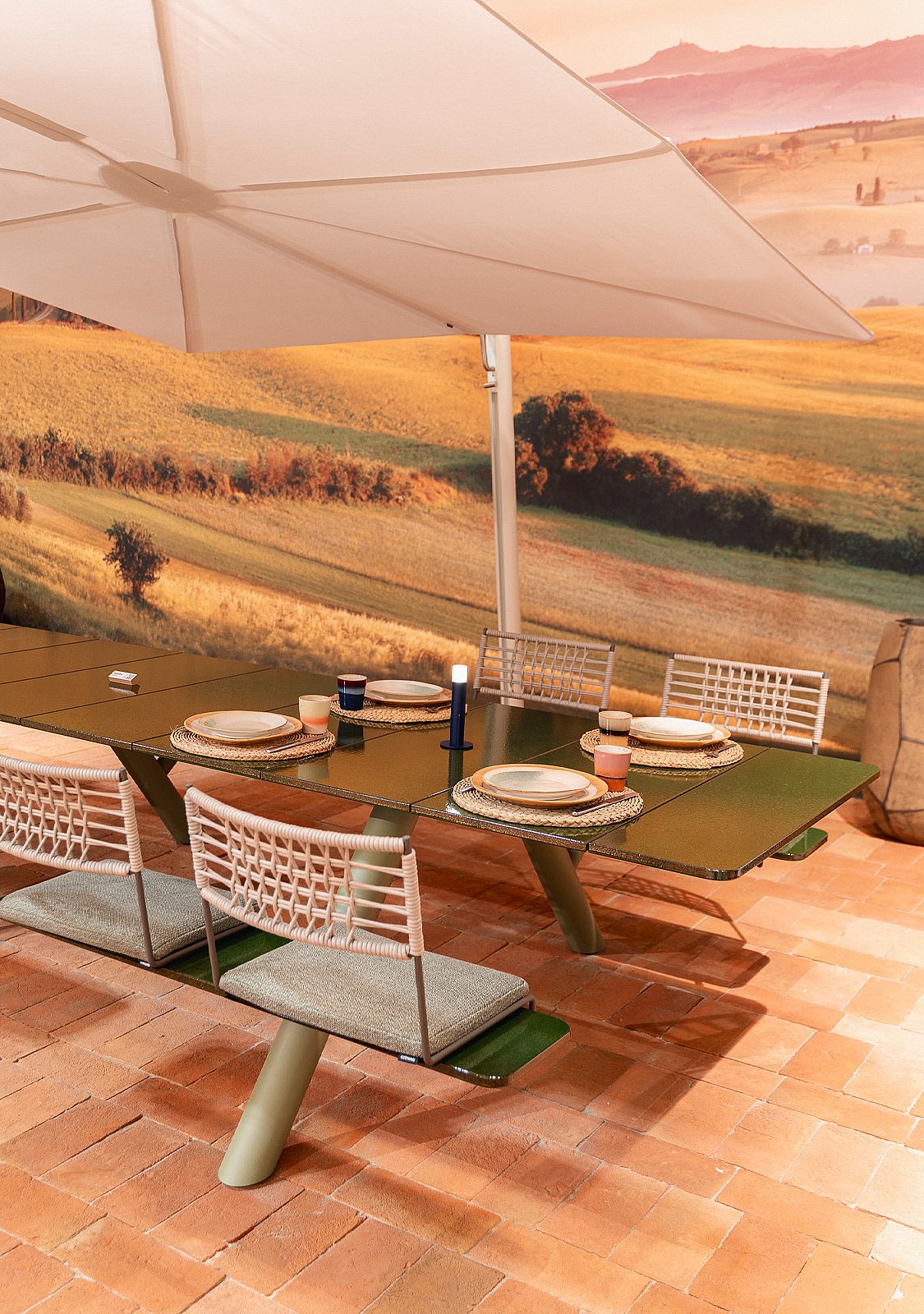 Groene modulaire Panigiri Lava eettafel bezet met geweven stoelen, borden, kaarsen en een grote witte parasol boven het hoofd.