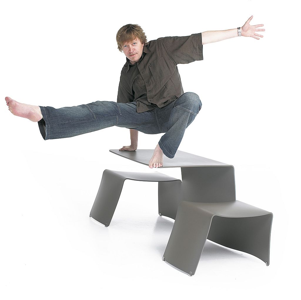 Designer Dirk poses barefoot on top of a grey Picnik table in a studio shot, demonstrating the strength and stability of the folded aluminium structure.