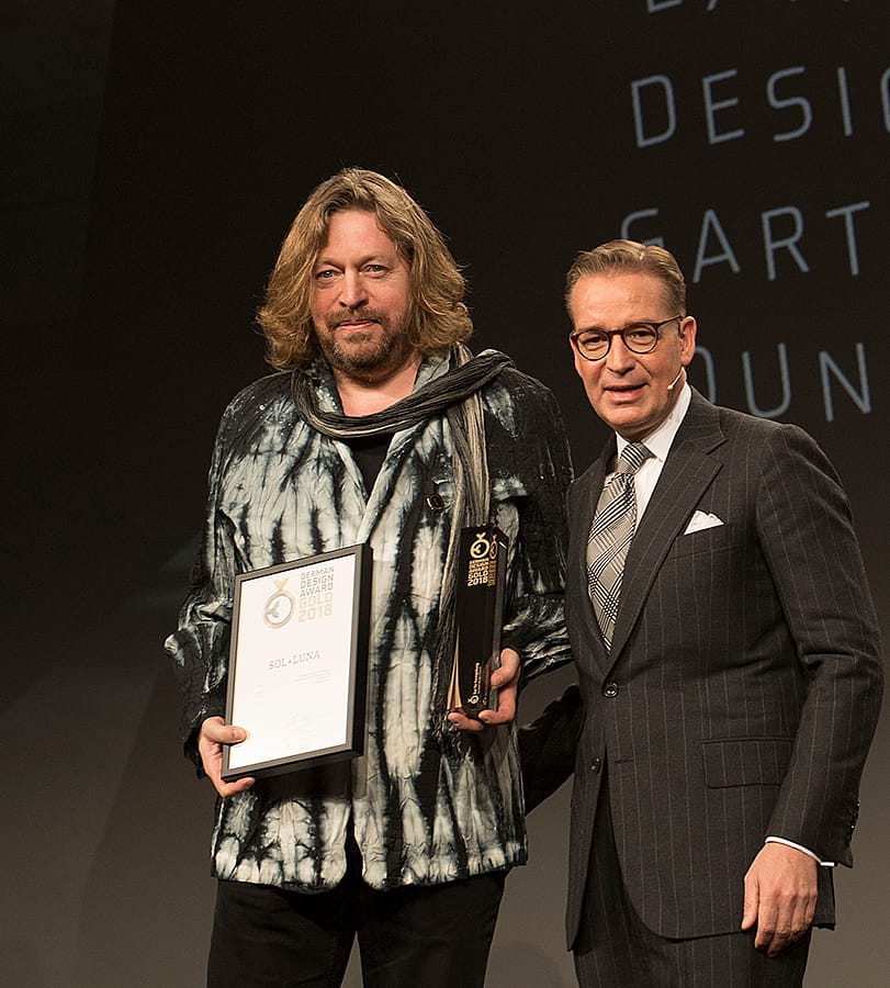 Dirk Wynants steht während der Preisverleihung in Frankfurt mit der Trophäe und Urkunde des German Design Award neben einem Mann im dunklen Anzug auf der Bühne.