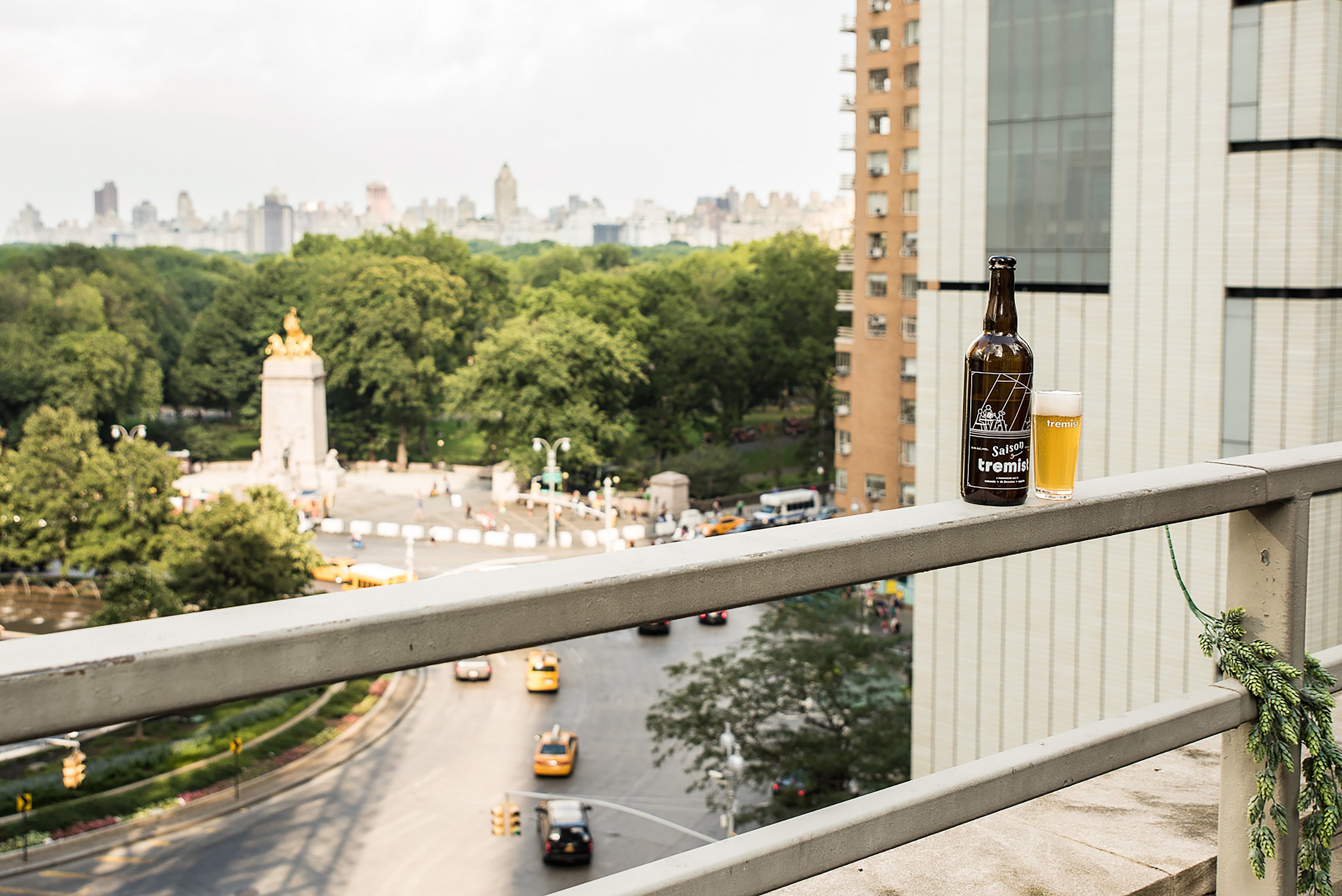 Bouteille et verre de bière Tremist placés sur la corniche du toit avec une vue panoramique sur Central Park et le rond-point en contrebas.