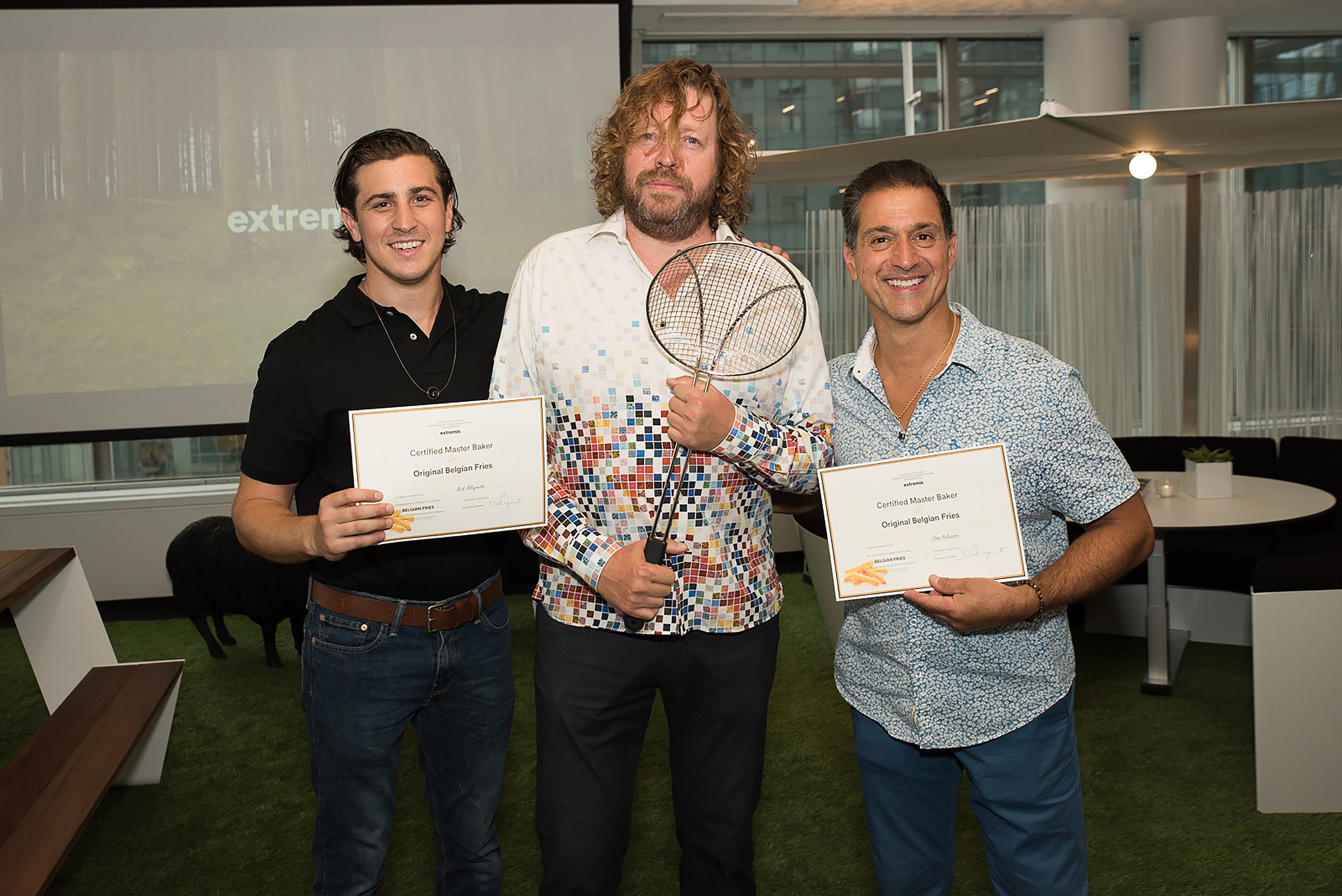 Dirk se tient entre deux hommes qui détiennent des diplômes et se félicitent mutuellement.