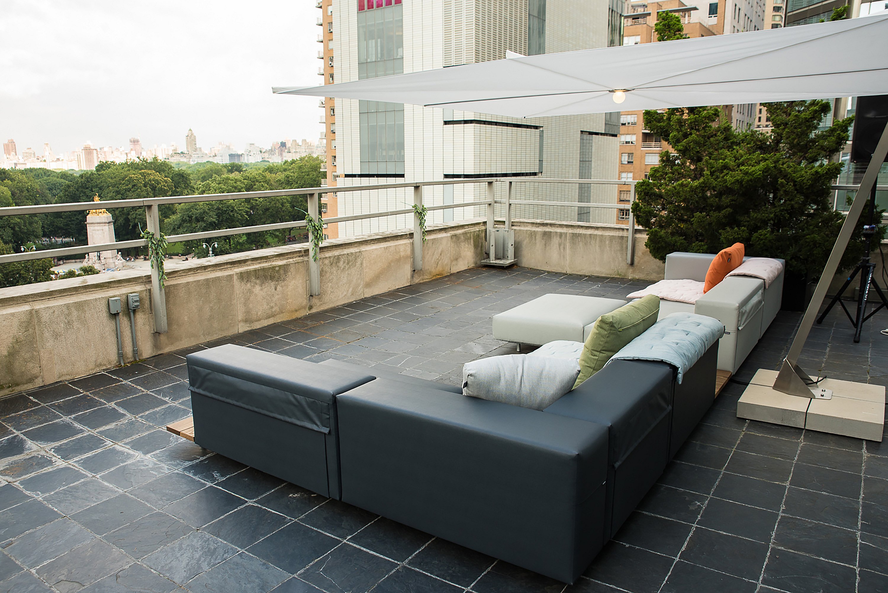 Grand salon extérieur modulable avec des coussins pâles sous une voile d’ombrage blanche étirée sur le toit-terrasse.