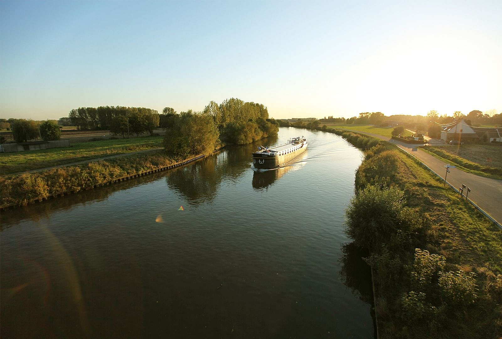 Cargo boat moving through a calm river landscape at sunset during the table’s journey to Kortrijk.